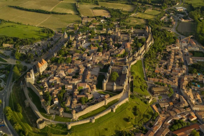 Aerial view of a walled medieval hilltop town with double stone ramparts and turrets amid green countryside