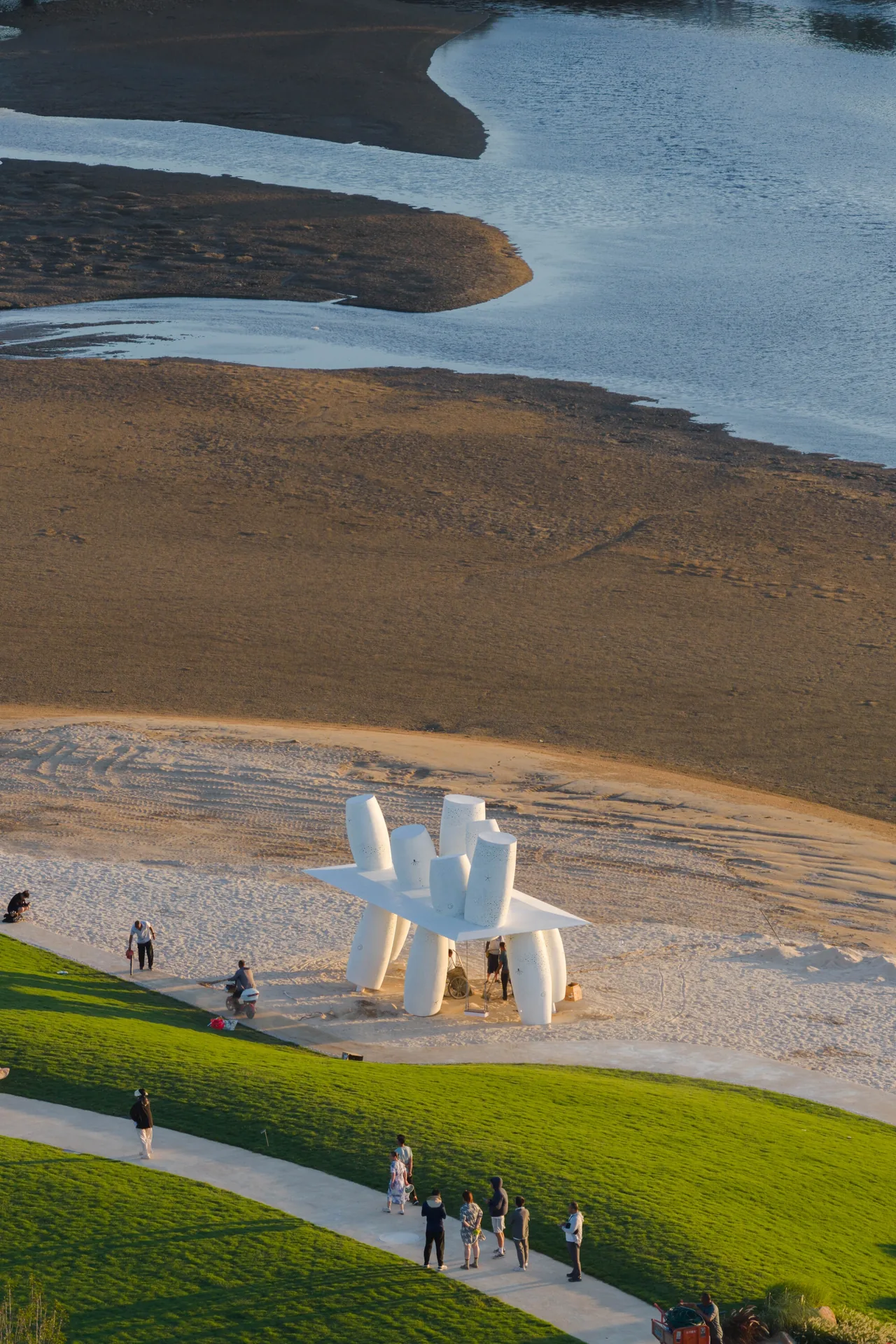 High view of the white structure on the sand between a lawn path and the tidal channels, Seaside Swing Installation by XBTW OFFICE