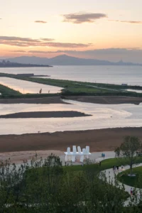 Sunset over the bay and tidal flats with the small white installation at the edge of the park, Seaside Swing Installation by XBTW OFFICE