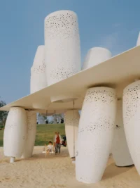 Low angle view up at the stacked cylinders and the edge of the roof plate with visitors beneath, Seaside Swing Installation by XBTW OFFICE