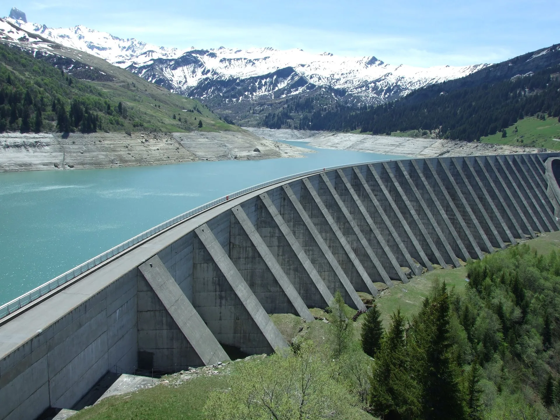 Concrete buttress dam holding back an alpine reservoir below snow-capped mountains