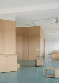 Pale MDF volume rising almost to the ceiling with a small trolley and stool on the green rubber floor, Aguacate Space by ALE Estudio