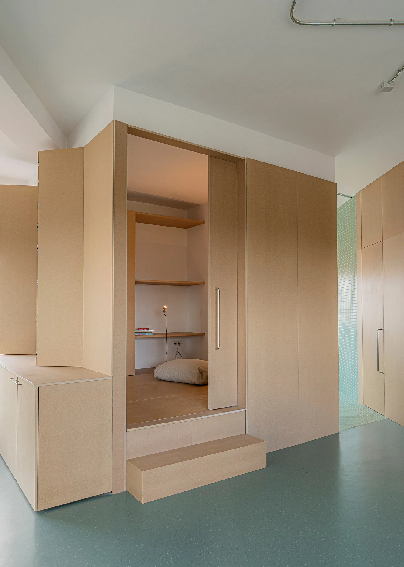 Raised wooden nook with a step, shelves and a floor cushion set into the timber volume, Aguacate Space by ALE Estudio