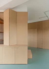 Tall pivoting timber panel beside cupboards and a wall of storage doors, Aguacate Space by ALE Estudio