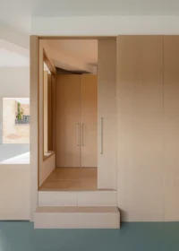 Doorway framed in wood leading up a step into a small wardrobe room, Aguacate Space by ALE Estudio