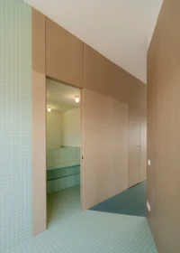 Mint tiled lobby with an open wooden door showing a lit bathroom inside the volume, Aguacate Space by ALE Estudio