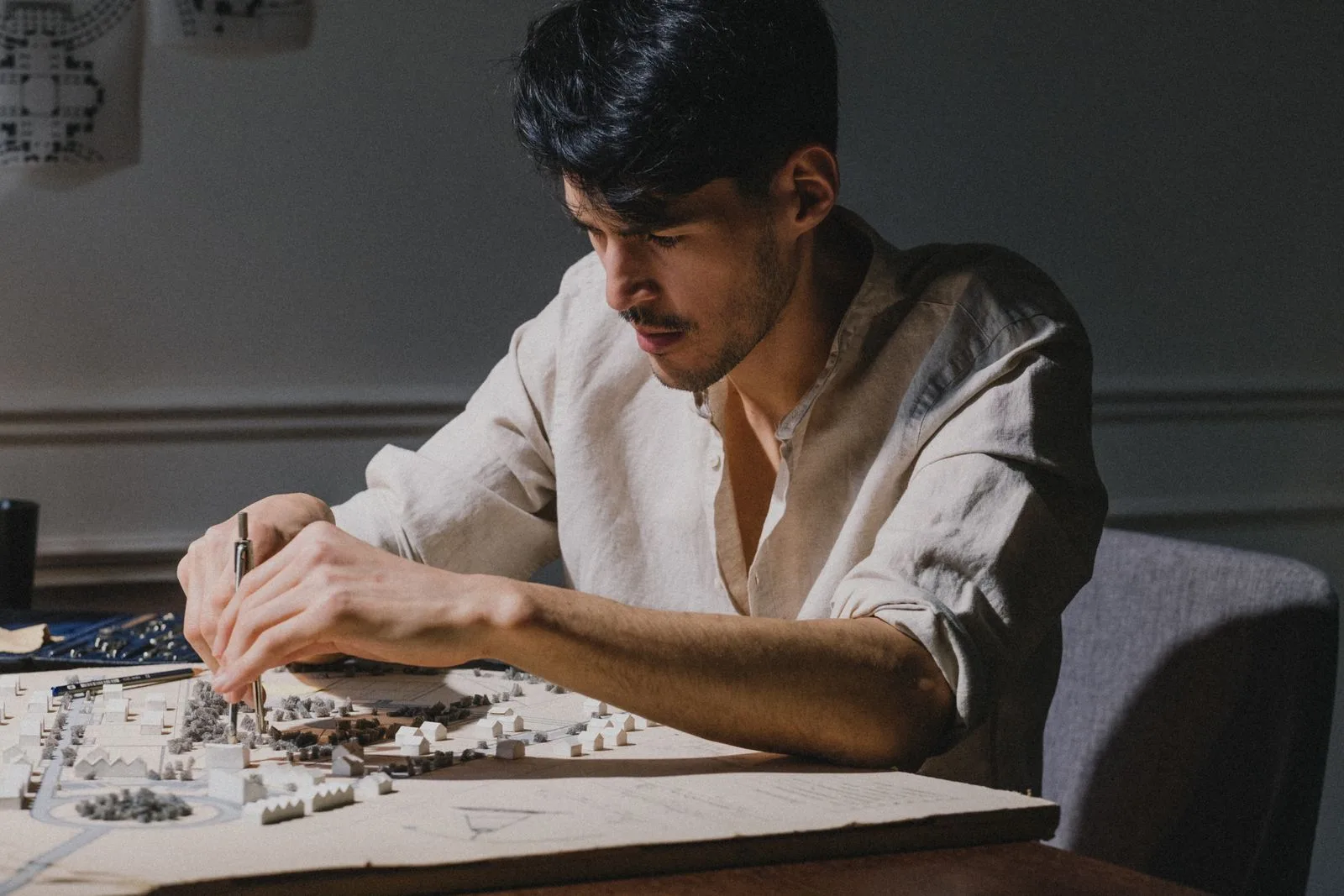 Young man assembling a detailed white architectural model with a tool under a desk lamp