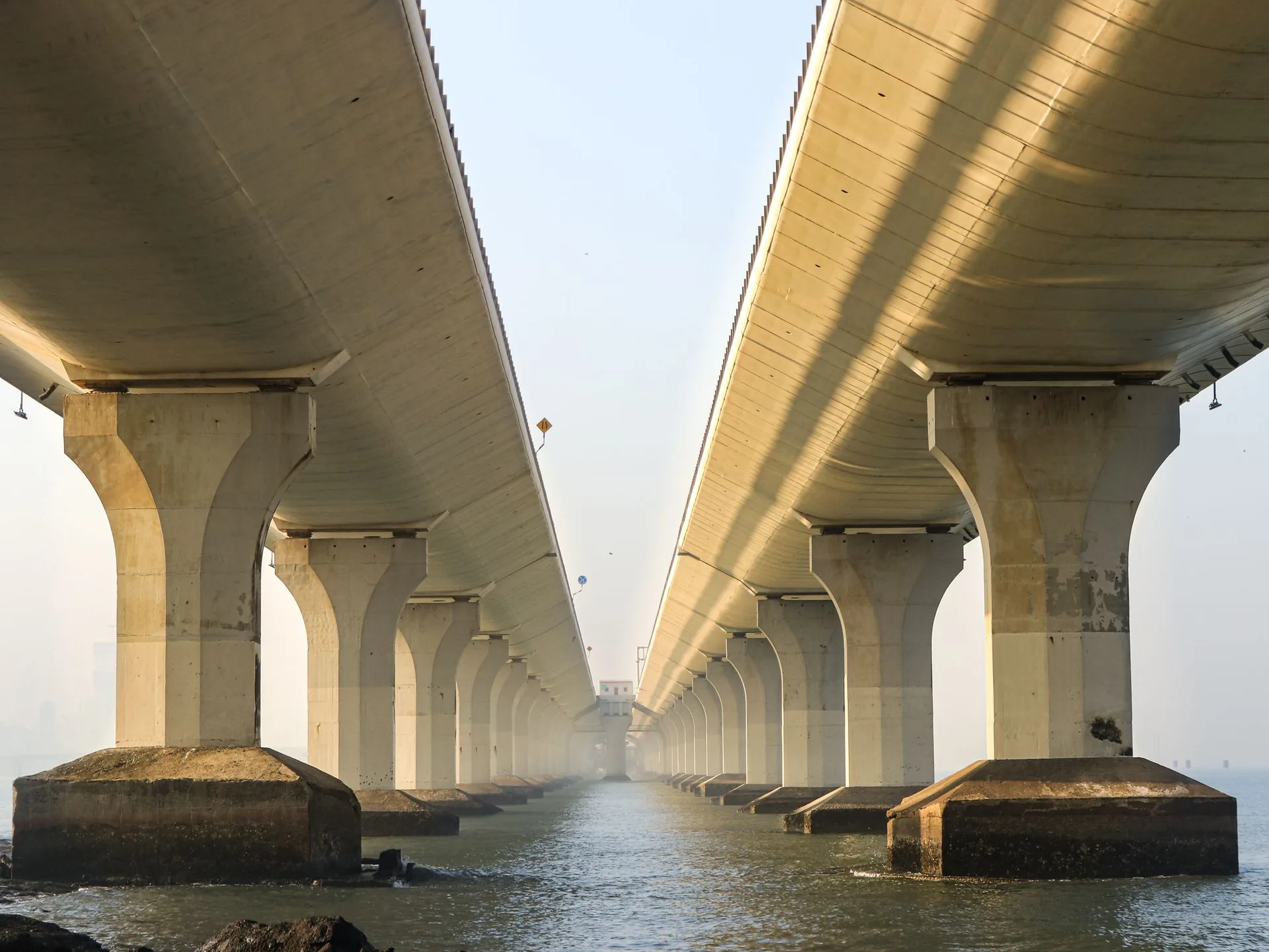 Underside of twin concrete bridge decks resting on rows of piers above water