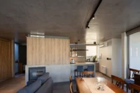Open plan interior with a timber clad kitchen block, sofa and dining table under a concrete ceiling