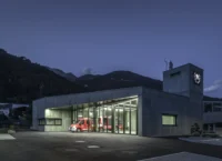 Fire station at dusk with its glazed vehicle bay lit up and a concrete hose tower carrying the brigade emblem, Civil Protection Centre by Roland Baldi Architects