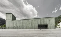 Long side elevation of the monolithic green volume rising from the tower toward the two storey end, Civil Protection Centre by Roland Baldi Architects