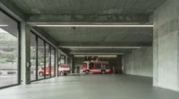 Vehicle bay with green concrete walls, a resin floor and fire engines parked behind full height glazing, Civil Protection Centre by Roland Baldi Architects