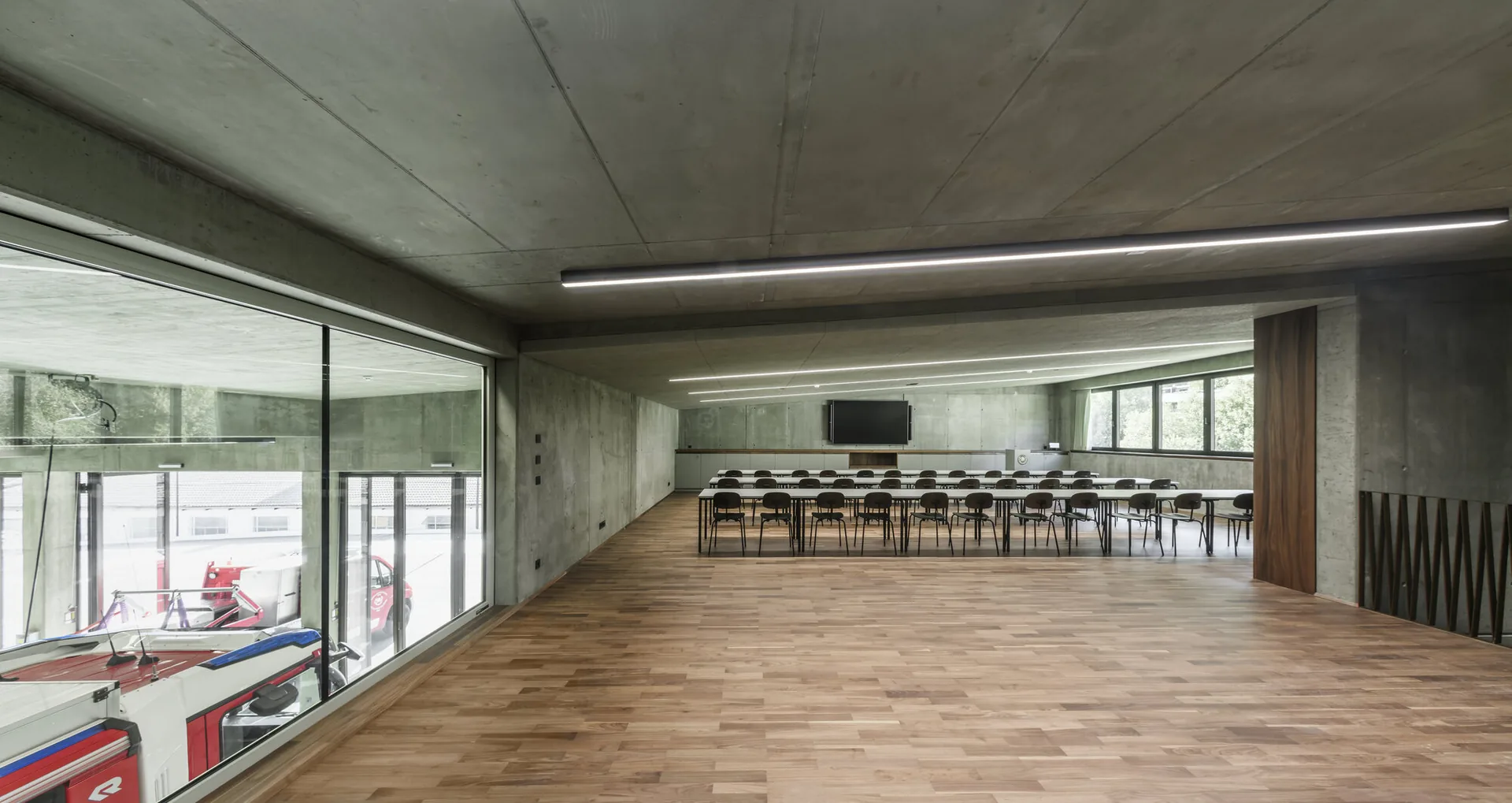 Upper floor lecture room with a timber floor and a large window looking down into the vehicle bay, Civil Protection Centre by Roland Baldi Architects
