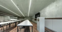 Lecture room with long white tables, linear ceiling lights, a timber floor and green concrete walls, Civil Protection Centre by Roland Baldi Architects