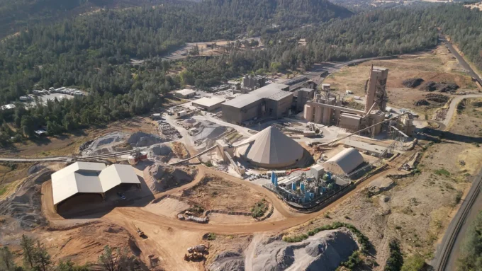 Aerial view of Fortera's Redding ReCarb plant, a cluster of blue silos set within a larger cement works in wooded hills