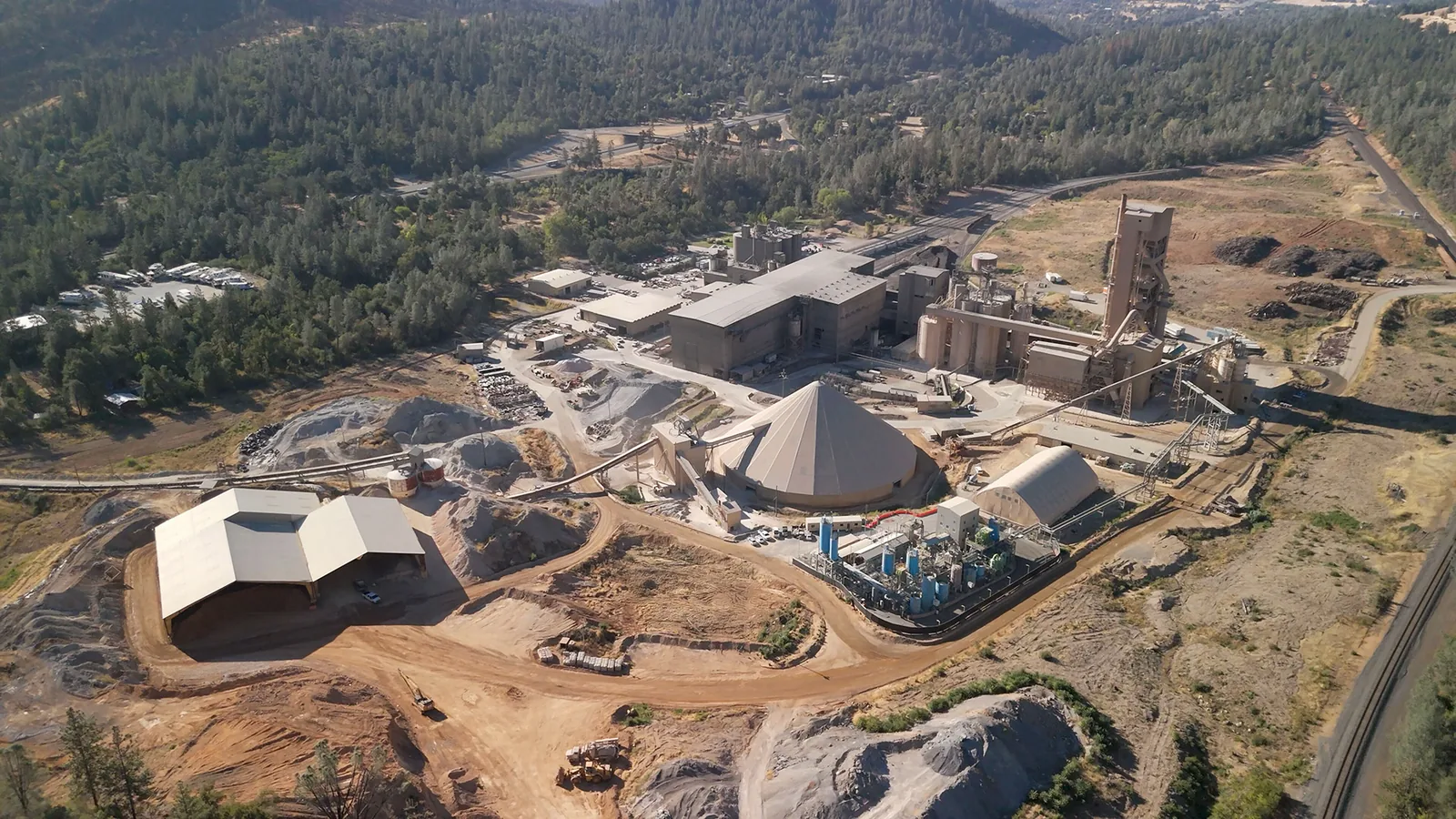 Aerial view of Fortera's Redding ReCarb plant, a cluster of blue silos set within a larger cement works in wooded hills