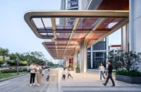 Curving canopy with a bronze underside sheltering a plaza where families walk, Greentown ThinkWorks