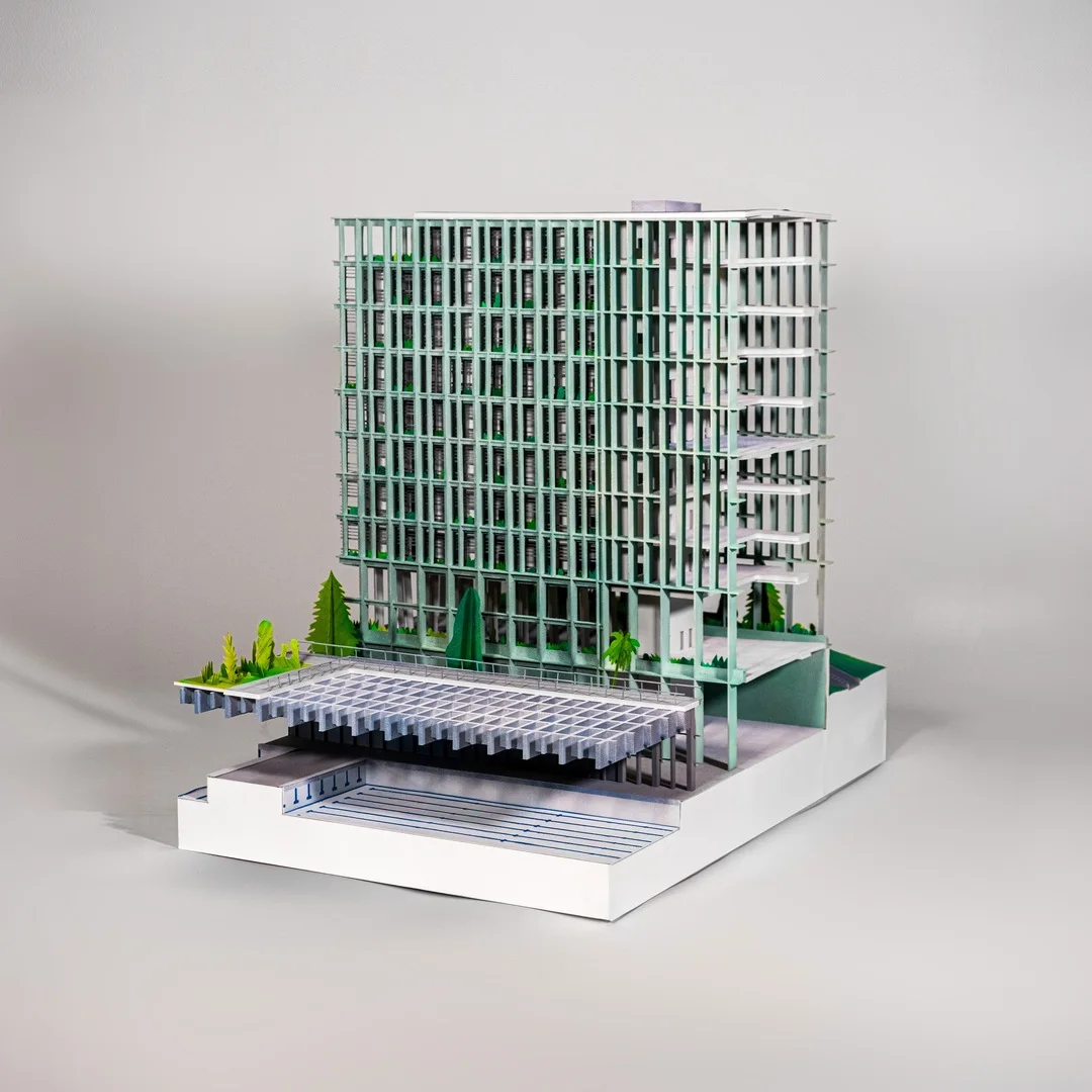 Photo of a white architectural model of a vertical healthcare tower on a display base, with finely crafted facade grid and planting
