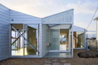 Corner of the house where two gabled volumes meet, with sliding glass doors, diagonal braces and stepping stones, House OY by 1-1 Architects