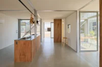 Interior with a long plywood kitchen counter, pale floor and a view through the house to a glazed door, House OY by 1-1 Architects