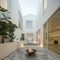 White courtyard open to the sky with planters, a fire bowl and tall glazing on both sides