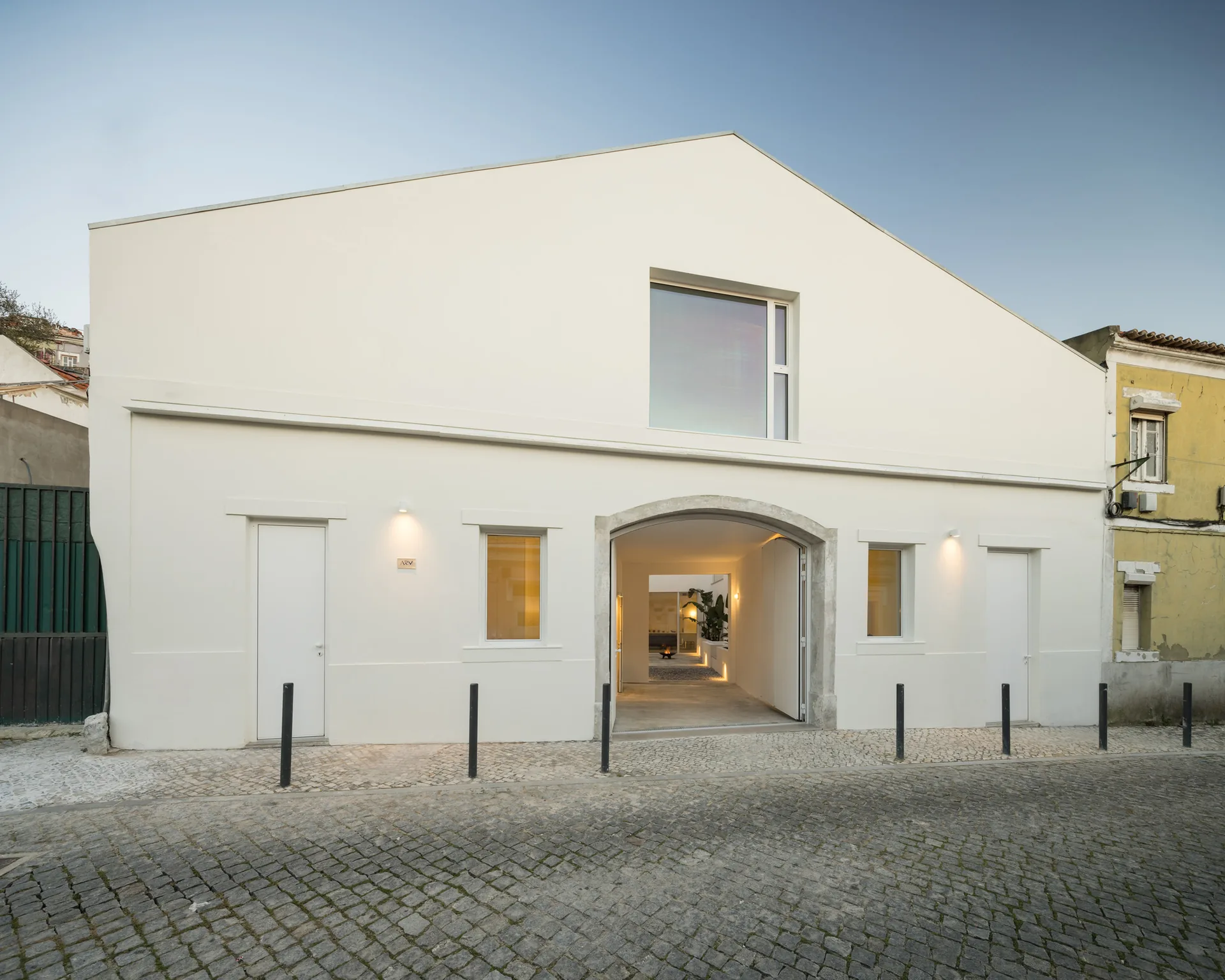 White gabled street facade with an arched entrance, small square windows and bollards on a cobbled street