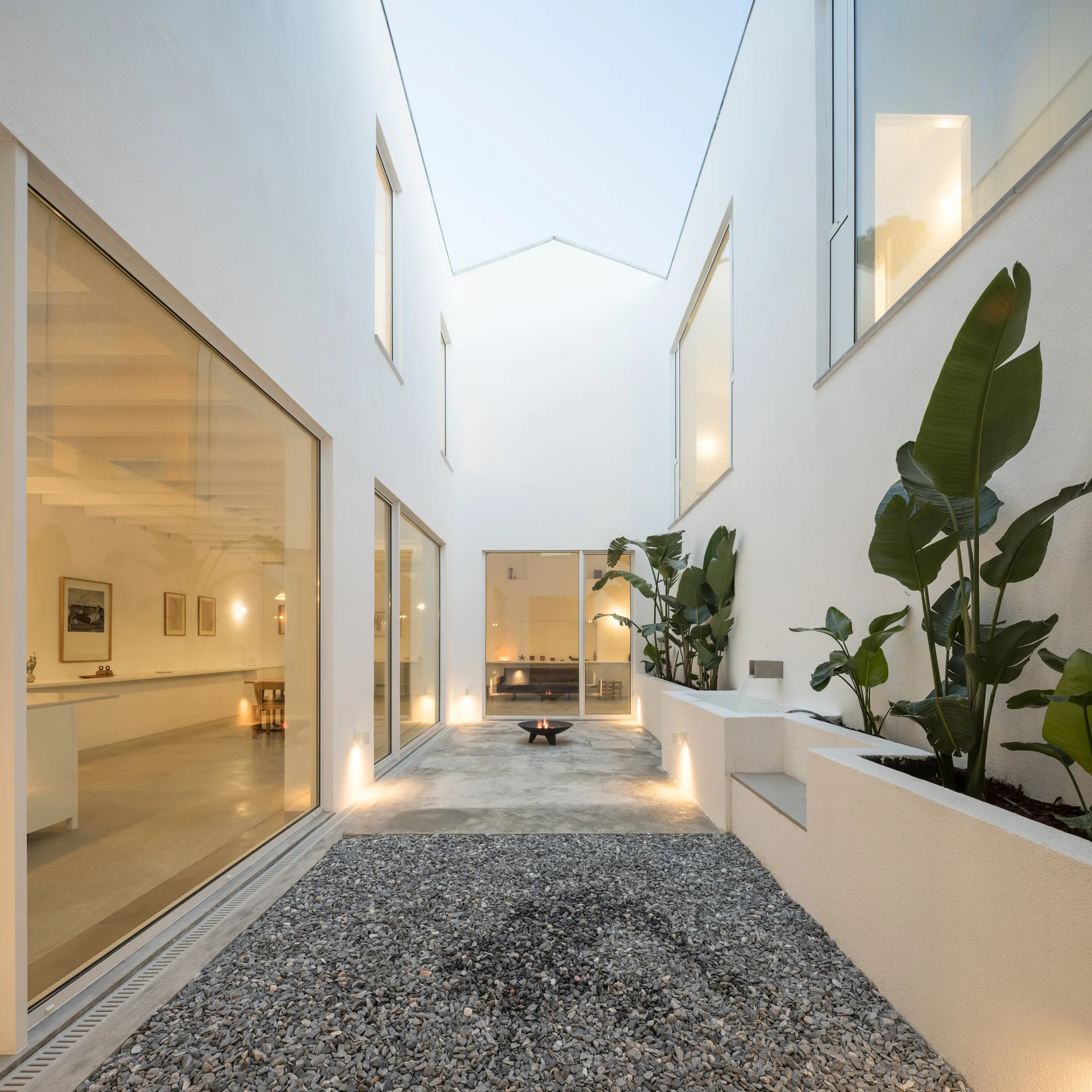 Gravel courtyard at dusk with large glass walls, planters and lights at ground level