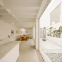 Kitchen island and dining table beneath white ceiling joists next to the courtyard glazing