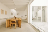 Rough timber dining table and chairs in a white room with a sliding glass wall