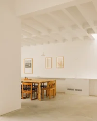 Dining area seen past a white wall with framed pictures and pendant lights