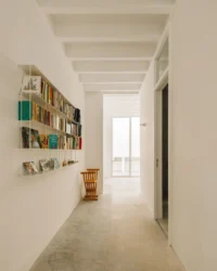 White corridor with wall mounted bookshelves leading to a bright doorway