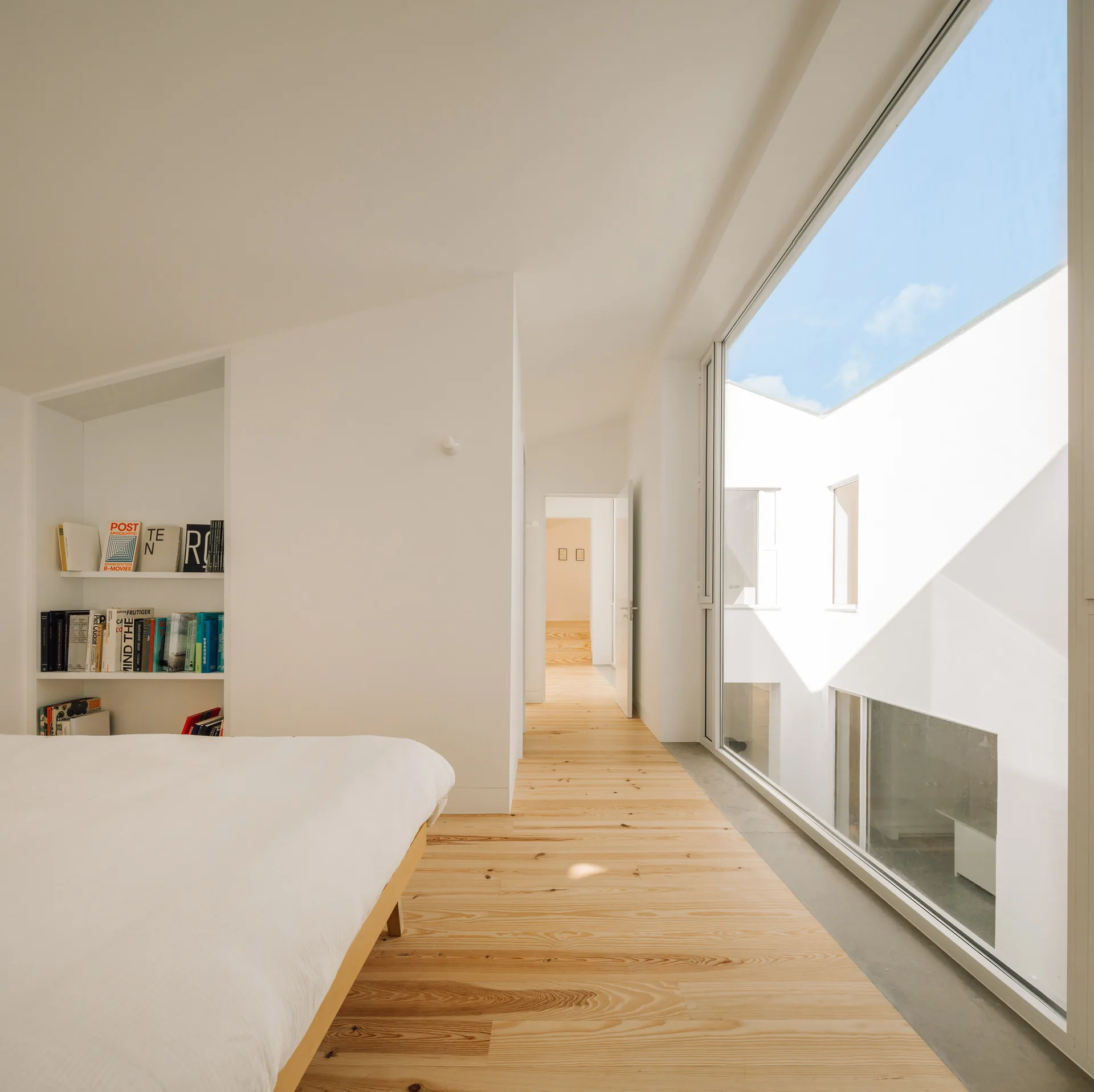 Upstairs bedroom with pine floorboards, a low bed and a wide window onto the white courtyard walls