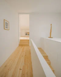 Upper landing with pine stairs, a white parapet and a slender timber sculpture