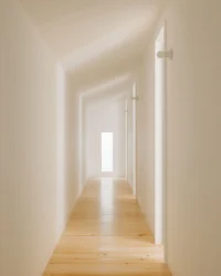 Narrow upper corridor with pine floor and a slot window at the end