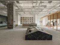 Black marble display block shaped like a house in an open store with a timber frame house and an artwork wall behind, Housing CARNIVAL by Studio Profile