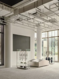 White columned retail area with a glass clothing cart, a low display plinth and a wall screen near the facade, Housing CARNIVAL by Studio Profile