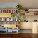 Living room bookcase on blue steel uprights beside a plywood kitchen counter with rattan stools