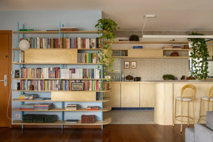 Living room bookcase on blue steel uprights beside a plywood kitchen counter with rattan stools