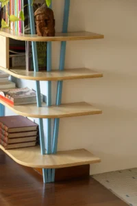 Curved plywood shelves stepping up a blue angled post at the end of the bookcase