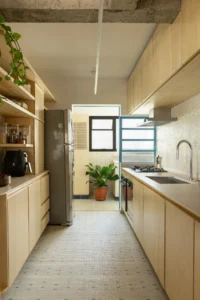 Narrow galley kitchen lined with plywood cupboards and a patterned tile floor leading to a window