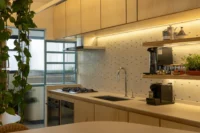 Kitchen worktop with gas hob, coffee machine and open shelves lit along a speckled tile wall