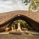 Front of the reception pavilion with a curling shingled roof arching over an open lounge and stepped timber platform