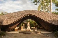 Front of the reception pavilion with a curling shingled roof arching over an open lounge and stepped timber platform
