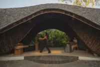 Guest walking beneath the wave shaped roof past a bench and a round reception desk