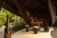 Round timber reception table with stools and a suitcase under the dark woven bamboo shell