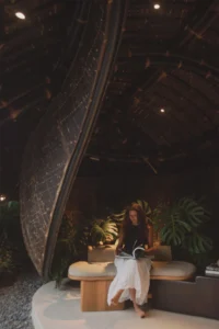 Woman reading on a bench beneath the tall curving bamboo wall lit by small downlights