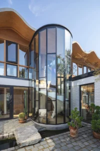 Curved glass stair tower between white brick walls and timber clad volumes under a rippling roof, Los Navegantes House