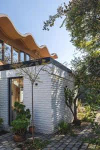 White painted brick wing with a planted path below the scalloped timber roof overhang, Los Navegantes House