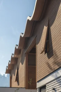 Upward view of vertical timber cladding and the scalloped roof eave against a blue sky, Los Navegantes House
