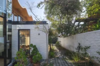 Narrow side garden with cobbles and potted plants between the brick wing and a white boundary wall, Los Navegantes House